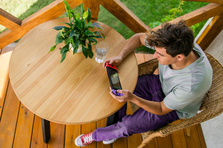 Young man playing video game drinking water at terrace in summer day.の写真素材