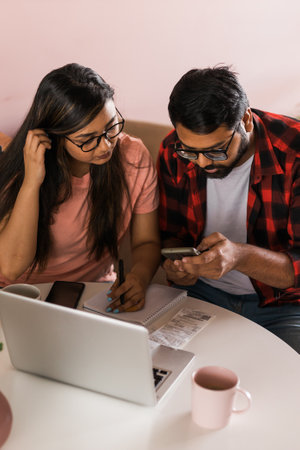 Serious wife and husband planning budget, checking finances, focused young woman using online calculator and counting bills or taxes, man using laptop, online banking services. Family sitting at table in kitchen - economic crisis conceptの写真素材