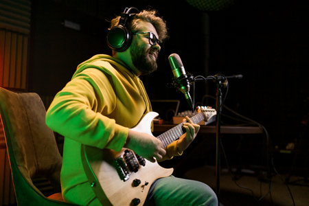 Male singer recording songs by using a studio microphone and and playing guitar in a music recording studio. Performance and show in the music business, streaming and recording music.の写真素材