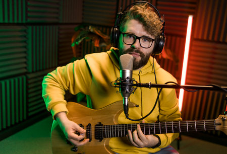 Male singer recording songs by using a studio microphone and and playing guitar in a music recording studio. Performance and show in the music business, streaming and recording music.の写真素材