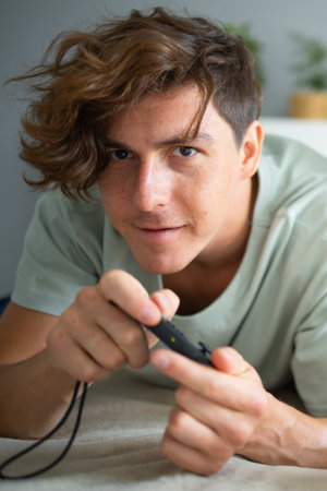 Portrait of handsome excited gamer lying on a bed and playing video games on a console. Wireless controller and online game technologies conceptの写真素材