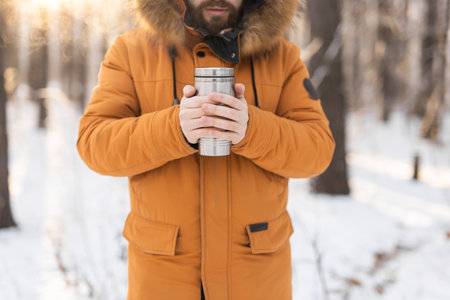 Man holding thermos in snowy forest during winter morning. Hot tea, comfort and mindfulness during a cold season outdoor activityの写真素材