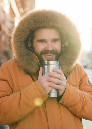 Man enjoying warm drink in sunlight on cold winter urban street. Peaceful solitude and morning routine in a winter city environment.の写真素材