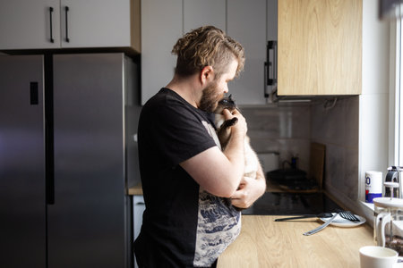 Man interacting with cat on kitchen counter during morning routine. Domestic life, pet care, and the calm atmosphere of everyday momentsの写真素材