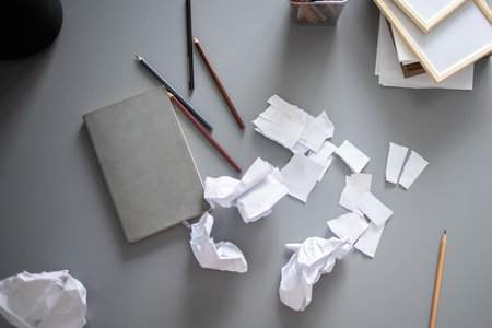 Messy home office desk with scattered paper and supplies. Creative block, frustration and domestic disorder in a modern living space.の写真素材