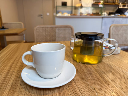 Glass teapot with herbal infusion and white ceramic cup on cafe table. Relaxation and modern tea cultureの写真素材