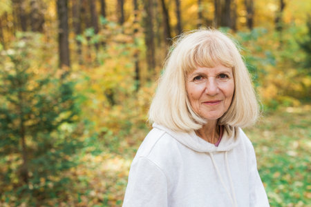 Mature woman close-up portrait in autumn forest and smiling peacefully. Emotional well-being and...