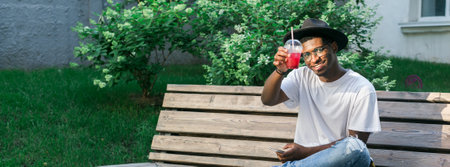 African american man enjoying a refreshing drink outdoors. Relaxation, leisure, and summer refreshment concepts. Banner with copy spaceの写真素材