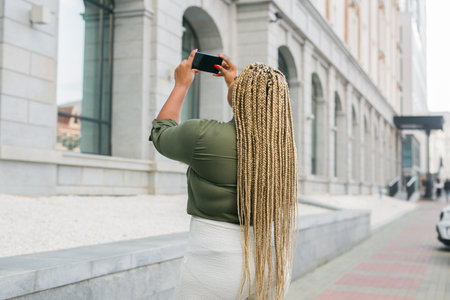 Affrican american woman taking a photo of a building with her smartphone. Tourism, sightseeing, and urban exploration momentsの写真素材