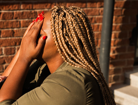 Woman covering her face with her hands in bright sunlight outdoors. Emotion, fatigue, and real human...