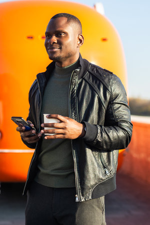 African american Man holding coffee and smartphone at a street food truck. Concept of travel, urban lifestyle and casual communication.の写真素材