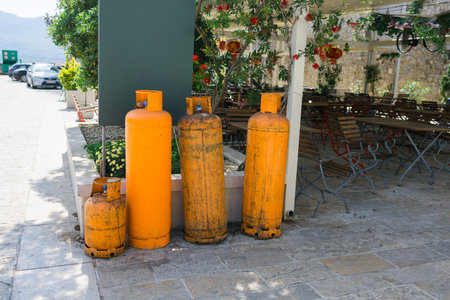 Outdoor storage of orange gas cylinders near cafe seating. Industrial utility, safety awareness, and restaurant operations.の写真素材
