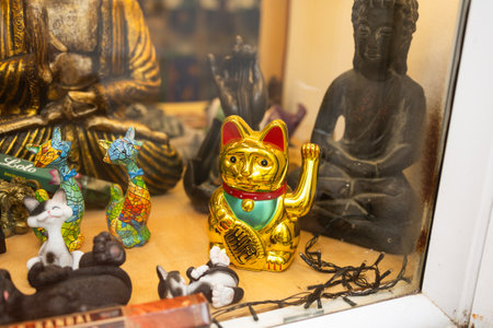 Lucky golden waving cat among colorful figurines and Buddha statues. Asian-inspired decoration, spiritual symbolism, and eclectic gift shop display.の写真素材