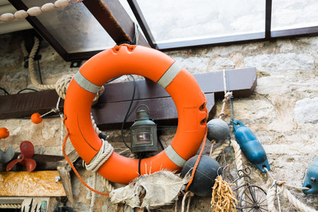 Orange lifebuoy with lantern and fishing props mounted on stone wall. Nautical atmosphere, maritime...
