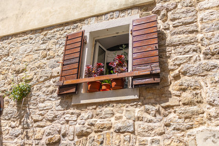 Rustic window with open wooden shutters and potted plants on stone wall. Mediterranean charm, urban...