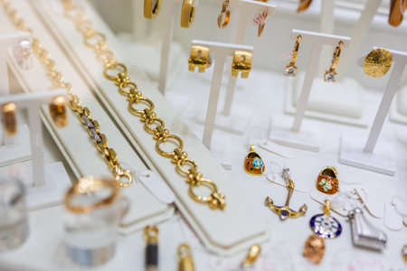 Gold bracelets, earrings, and charms arranged in jewelry store display. Luxury fashion, accessory detail, and elegant retail collection.の写真素材