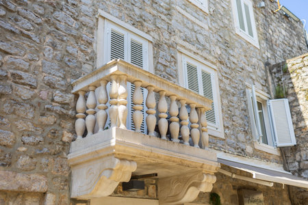 Old stone building with white balcony and closed shutters. Historic architecture with Mediterranean style, rustic charm, and warm sunlight.の写真素材