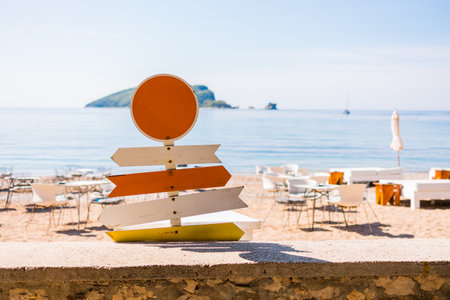 Wooden beach signpost with arrows on seaside promenade. Summer vacation, coastal leisure, and travel direction concept.の写真素材