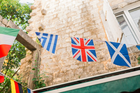String of international flags in a Mediterranean alley. Cultural diversity, travel spirit, and festive street decor in a sunlit stone village.の写真素材