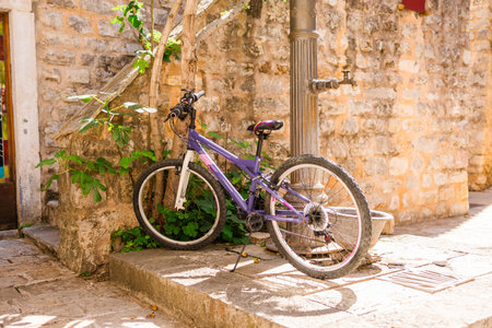 Purple bicycle resting near a vintage fountain in a Mediterranean alley. Casual transportation, timeless street charm, and rustic urban tranquility.の写真素材