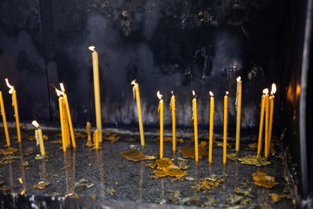 Lit candles in sand inside a church shrine. Spiritual ritual, personal prayer, and the quiet power of remembrance and sacred tradition.の写真素材