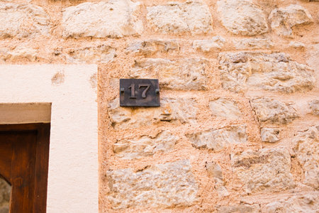 Number 17 plaque on rustic stone wall near wooden doorway. Summer travel, architectural heritage, and identification in old European towns.の写真素材