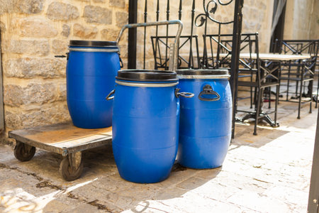 Three blue barrels beside outdoor cafe. Utility objects, urban logistics, and rustic courtyard...