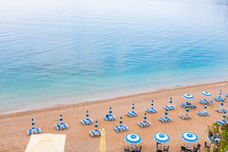 Tranquil morning at a beach with blue umbrellas and loungers. Coastal vacation, summer relaxation and peaceful seaside tourism.の写真素材