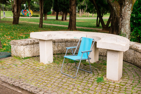 Lonely blue chair by a stone table in a city park. Urban solitude, quiet outdoor moment and everyday still life.の写真素材