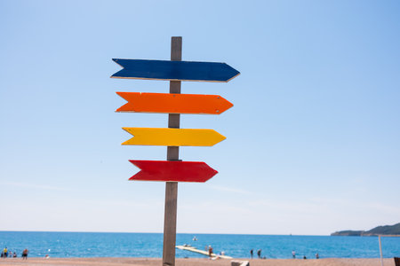 Wooden beach signpost with arrows on seaside promenade, copy space. Summer vacation, coastal leisure, and travel direction concept.の写真素材