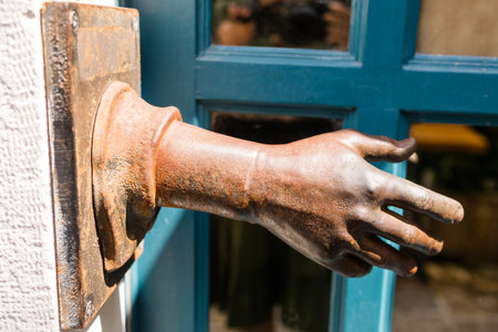 Rusty sculpted hand emerges from a wall beside a blue wooden door. Artistic urban decor, surreal visual element, and unique street detail in Budva, Montenegro.の写真素材