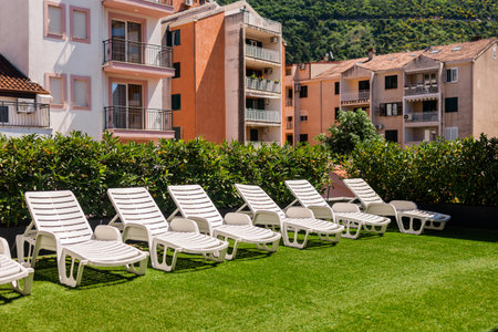 White lounge chairs on artificial grass rooftop. Urban sunbathing, summer relaxation, and outdoor leisure in residential neighborhood.の写真素材