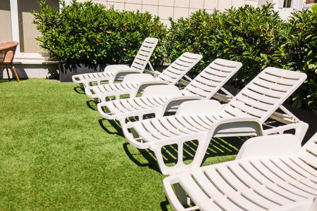 White lounge chairs on artificial grass rooftop. Urban sunbathing, summer relaxation, and outdoor leisure in residential neighborhood.の写真素材