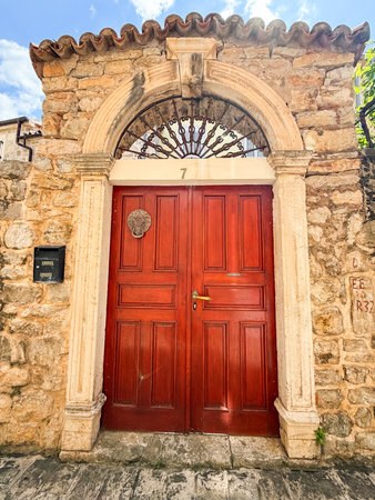 A red wooden double door with arched stone frame and decorative details on facade. Tradition, architecture, entrance and identity in historic urban residential design.の写真素材