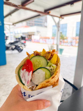 Hand holding gyro with vegetables, fries and sauce. Food, cuisine, street meal and Mediterranean gastronomy in urban lifestyle.の写真素材