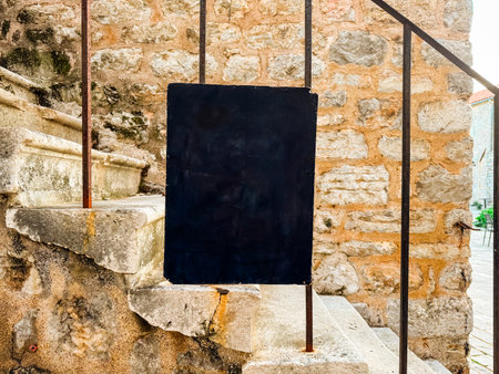 Empty black signboard on stone wall steps. Urban identity, communication and cultural heritage in a historic old town environment. Copy spaceの写真素材