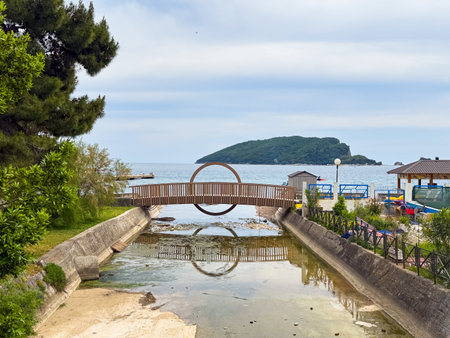 Wooden bridge with circular design reflected in water facing small island in sea. Travel, tourism, architecture, leisure and scenic coastal destination with unique design.の写真素材