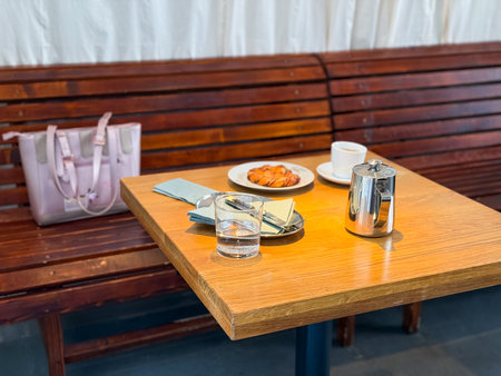 Coffee and pastry on wooden table next to pink bag. Breakfast, indulgence, and social cafe lifestyle.の写真素材