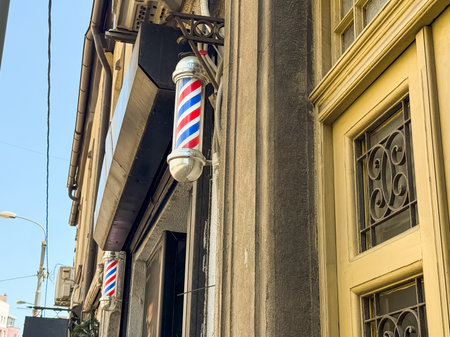 Traditional barber pole with red, blue and white stripes mounted on a wall. Urban tradition, retro style and classic grooming culture.の写真素材