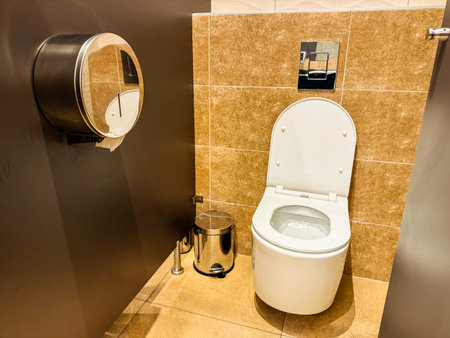 Public restroom interior with toilet and metal bin near tiled wall. Sanitation, hygiene, and facility design for cleanliness, comfort, and guest convenience.の写真素材