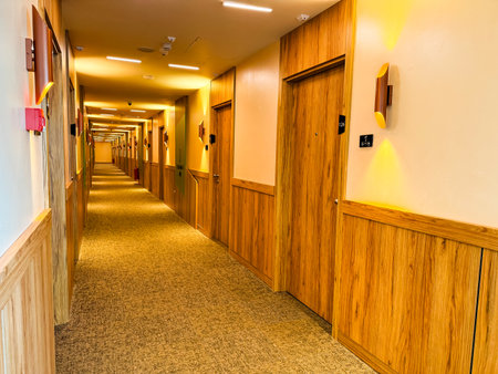 Long hotel hallway with aligned wooden doors and illuminated ceiling lights creating perspective view. Hospitality, travel, and architecture symbolizing interior design, order, and modern facility.の写真素材