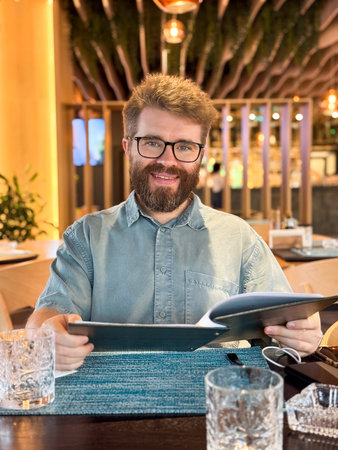 Man reading a menu in a modern restaurant interior. Everyday lifestyle, leisure, dining and customer experience in casual setting with contemporary design and atmosphere.の写真素材