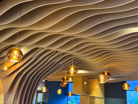 Decorative ceiling with golden lamps and wavy wooden structure in modern restaurant interior. Atmosphere, architecture, hospitality and contemporary design detail for lifestyle.の写真素材