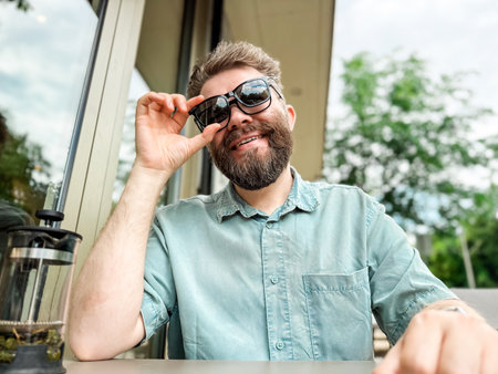 Glasses with magnetic clip on sunglasses. Man smiling while wearing clip on sunglasses at outdoor cafe tableの写真素材