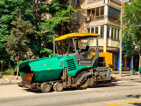 Road paver working on a street. Construction, urban infrastructure, and industrial machinery in city...