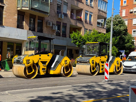 Row of road rollers on a city street. Heavy construction equipment, infrastructure, and maintenance...