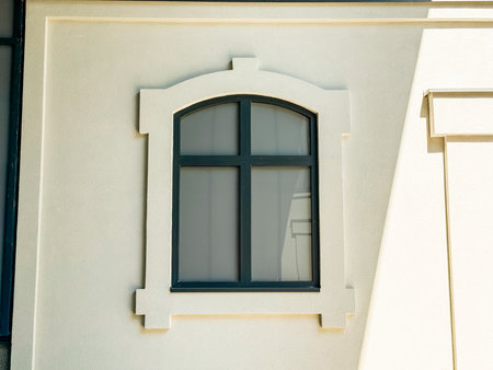 Window with decorative frame design placed on a light-colored building facade in sunlight....