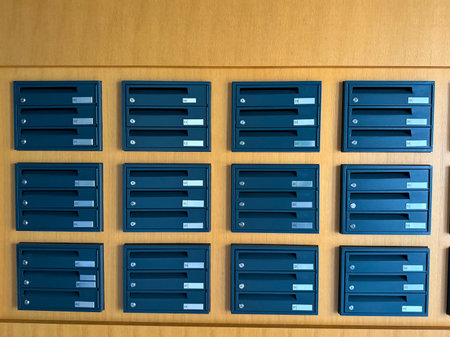 Row of numbered metal mailboxes installed on a wooden wall in residential building. Communication, infrastructure and housing facility representing organization, delivery and correspondence service.の写真素材