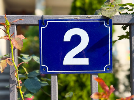 House number plate with digit two on fence. Orientation, address, and identification in urban...