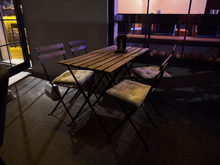 Outdoor wooden table with folding chairs and cushions at night terrace. Hospitality, leisure, and...
